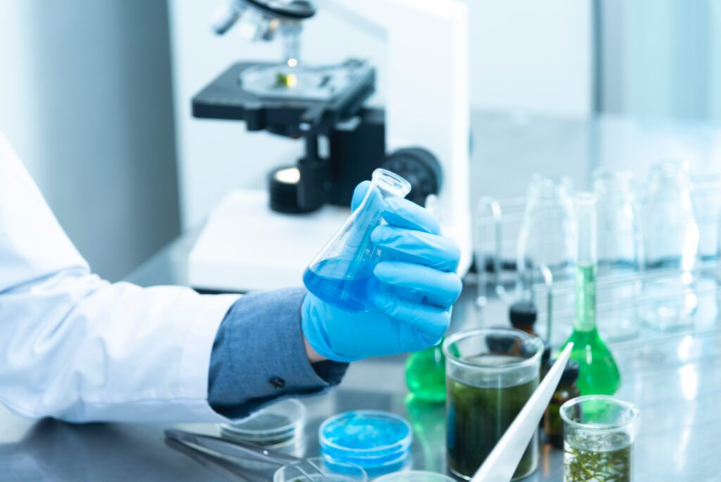 Eine Person befindet sich in einem Labor und hält ein Reagenzglas mit blauer Flüssigkeit in der Hand